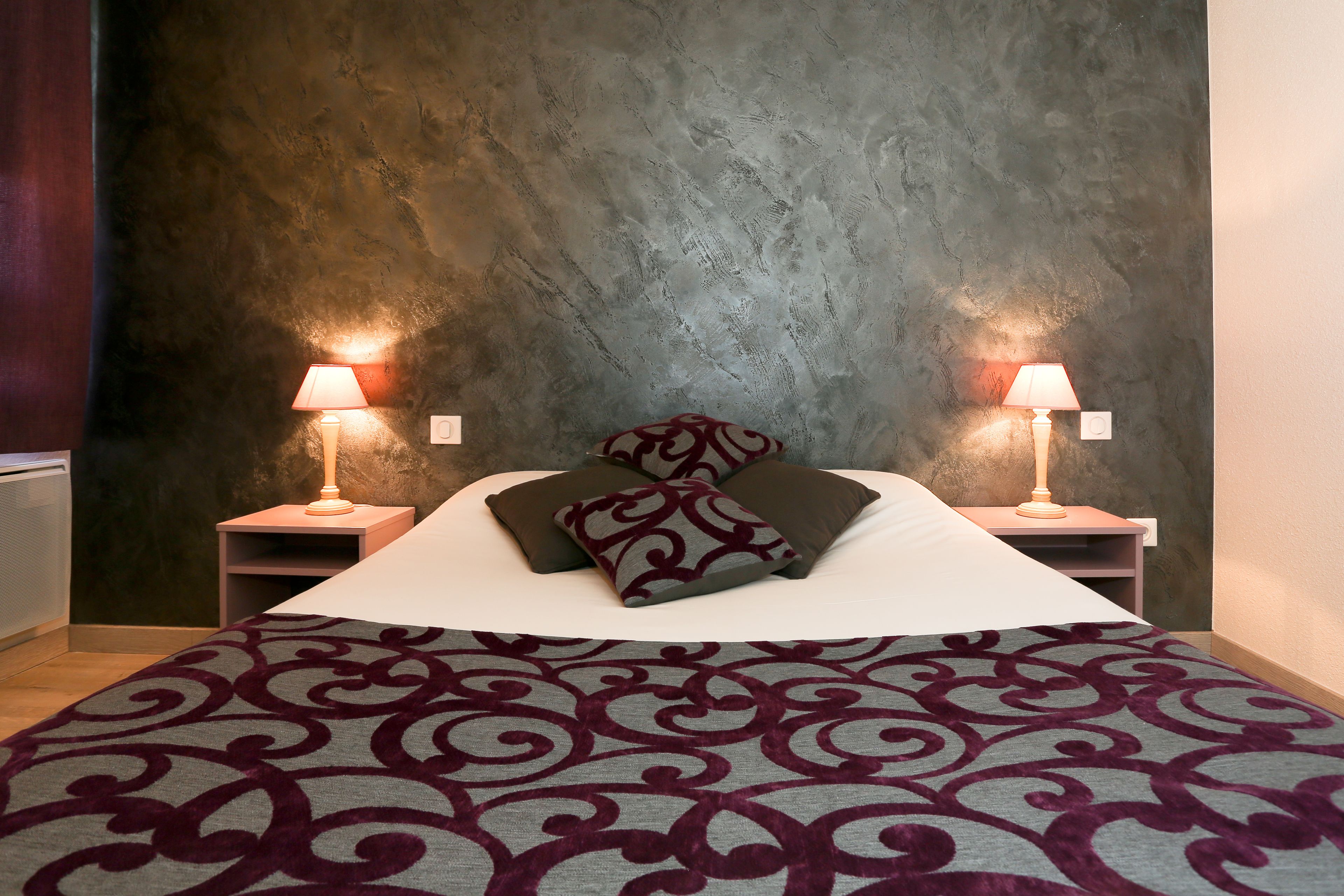 A neatly made bed with a patterned bedspread, two bedside lamps, and a textured wall behind.