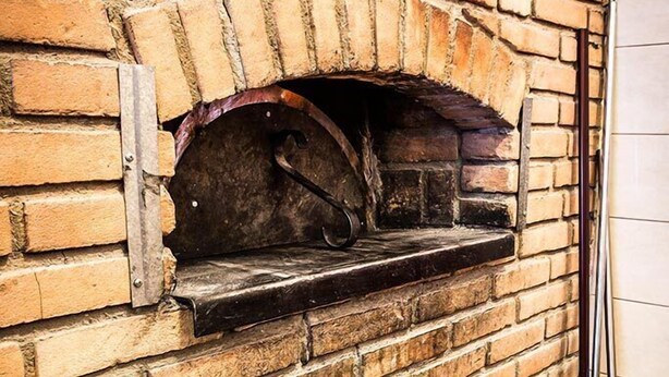 A brick fireplace with a wood-burning stove, a chimney, and a fire shovel. - Due Platani (Airuno)