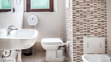 Un baño moderno con lavamanos, inodoro y bidé, una ventana y un revestimiento de pared estampado.