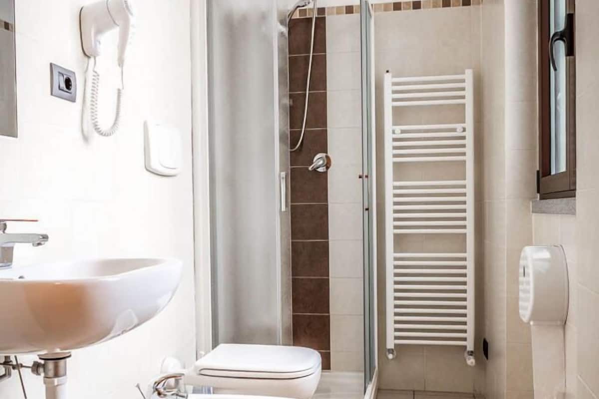Un baño con lavamanos, bidé, inodoro, ducha y toallero.