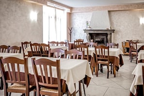 A dining area with wooden chairs and tables, a fireplace, and a view of the outdoors. - Due Platani (Airuno)