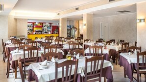 A restaurant with multiple tables and chairs, a bar area in the background, and a door leading to another room. - Due Platani (Airuno)