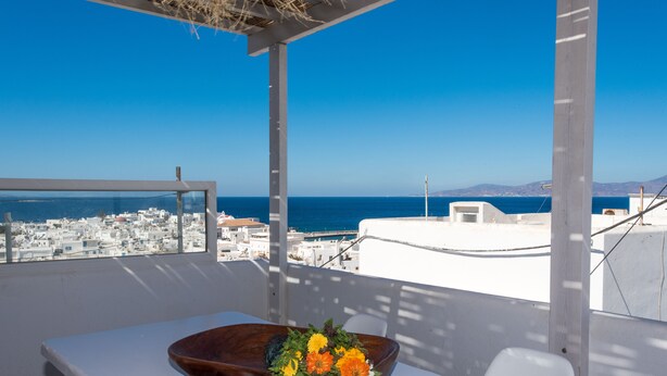 Un balcón con una mesa, un cuenco de madera con flores y vistas al mar y a la ciudad.