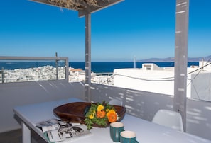 Un balcón con una mesa, un cuenco de madera con flores y vistas al mar y a la ciudad.