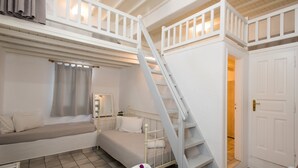 Una habitación con cama tipo voladizo, una escalera y una puerta que da a otra habitación.