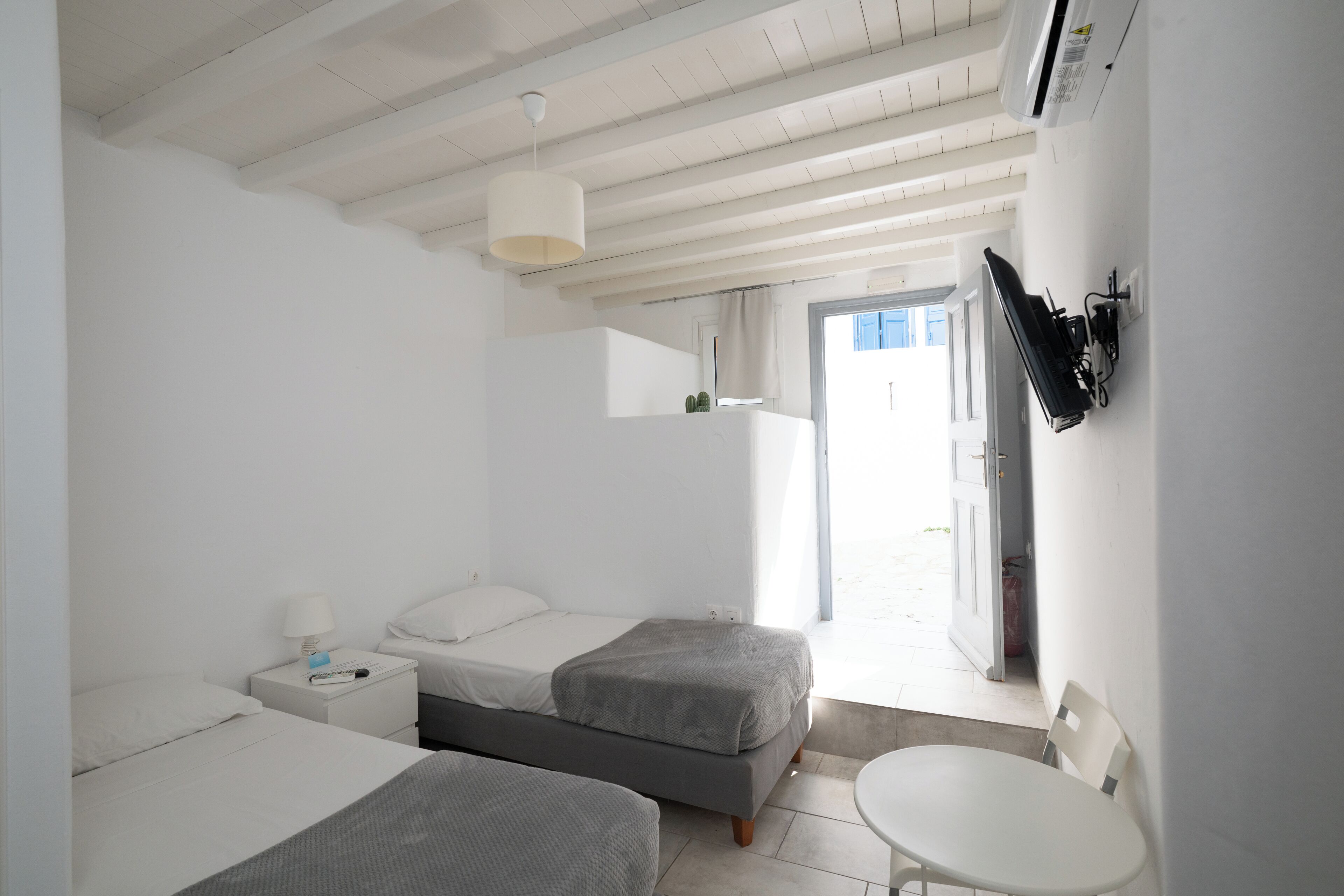 A modern hotel room with two beds, a small table, and a view of the outdoors.