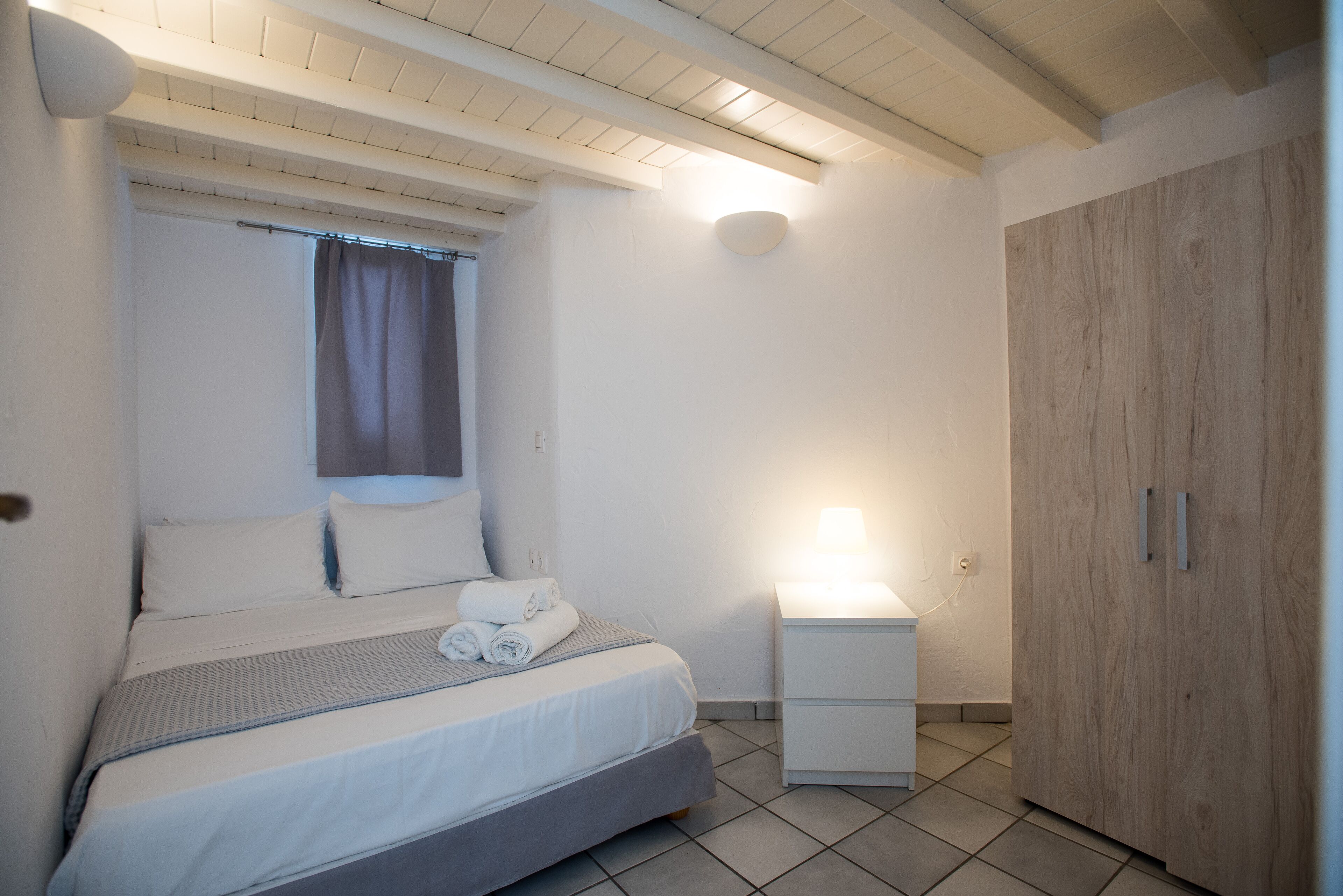 A bedroom with a bed, a nightstand, a wooden wardrobe, and a ceiling light.