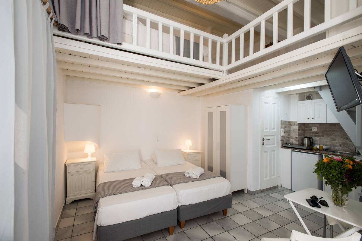 A bedroom with two beds, a small kitchenette, and a balcony.