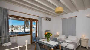 Una habitación con cama, una mesa de comedor con sillas, una pequeña mesa con un florero y vistas a un pueblo costero.
