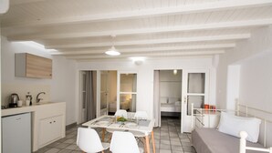 Una cocina compacta y moderna con armarios blancos, una mesa de comedor con cuatro sillas y una cama con cabecera blanca.