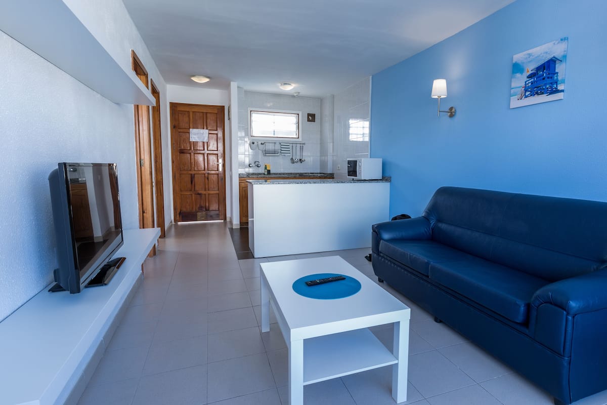 Ein modernes Wohnzimmer mit einem blauen Sofa, einem weißen Couchtisch und einem Flachbildfernseher.