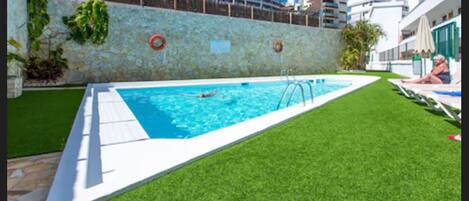 Una piscina al aire libre, sombrillas, sillones reclinables de piscina