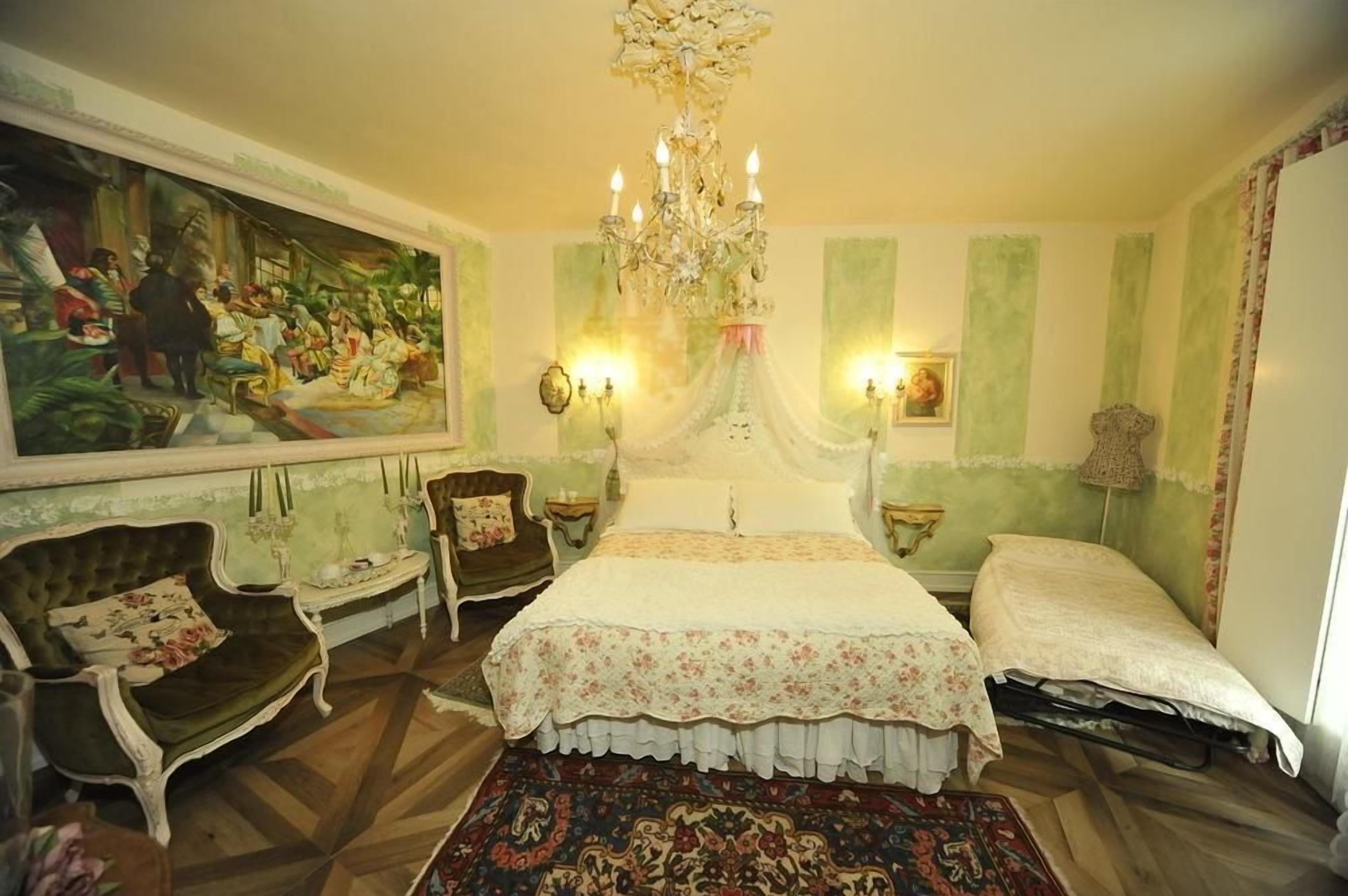 Een kamer met een groot bed, twee stoelen, een kroonluchter en een schilderij aan de muur.