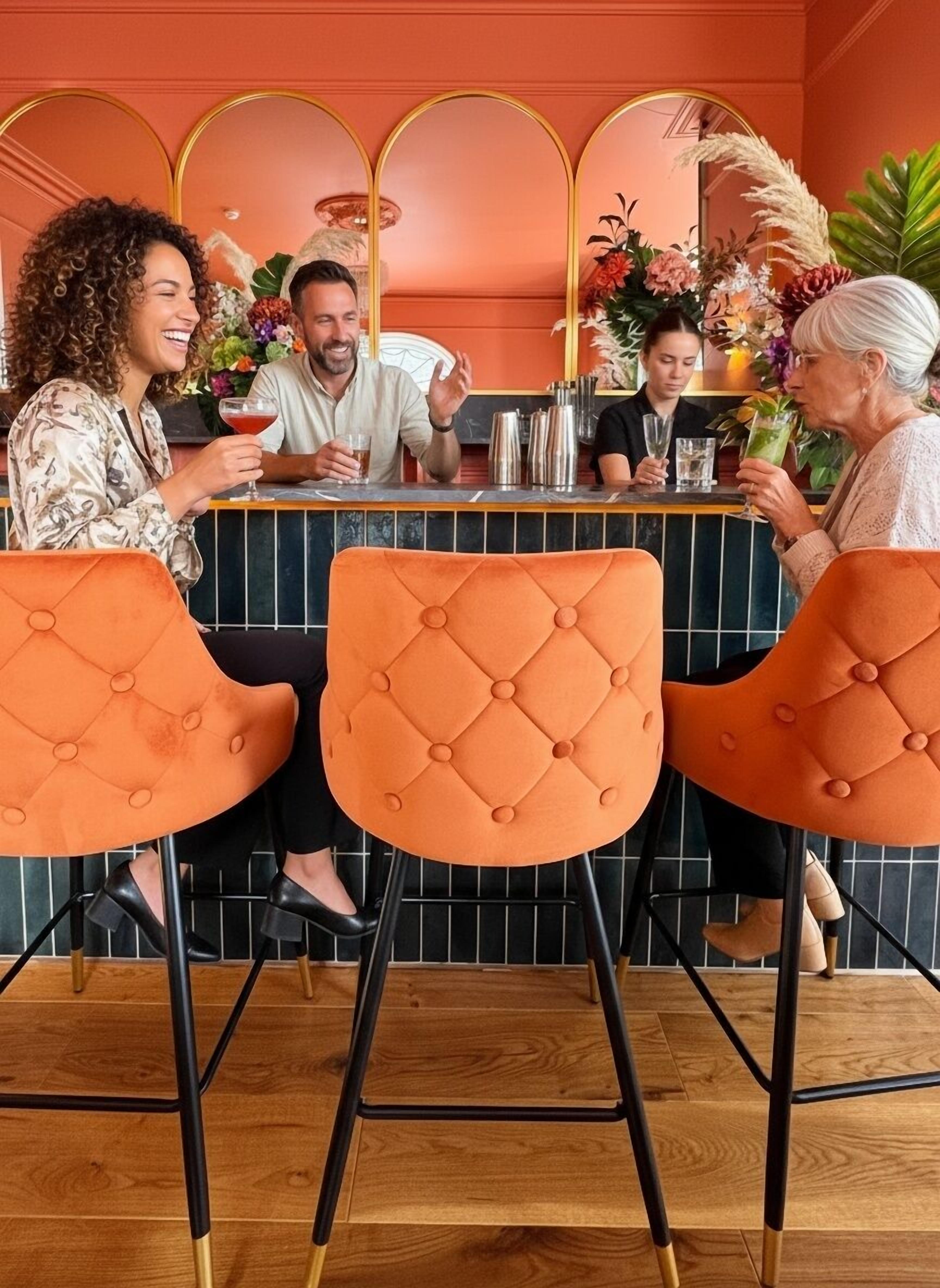 A bar area with orange upholstered chairs, a counter with a mirror, and a wooden floor.