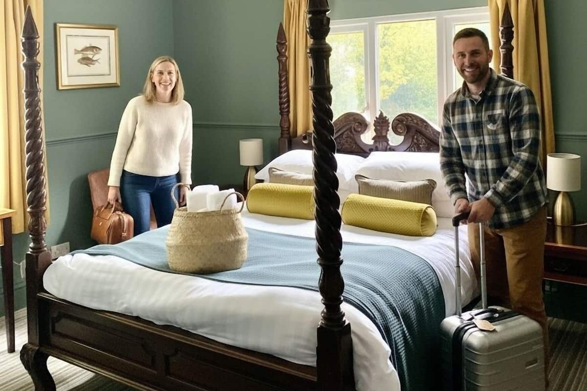 A four-poster bed with a wooden frame, a bedside table with a lamp, and a window with curtains.