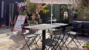 Un espacio al aire libre con mesas y sillas, un letrero que indica una sala de té y plantas decorativas.