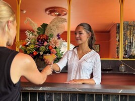 Una zona de bar con mostrador, un arreglo floral y un espejo que refleja la habitación.