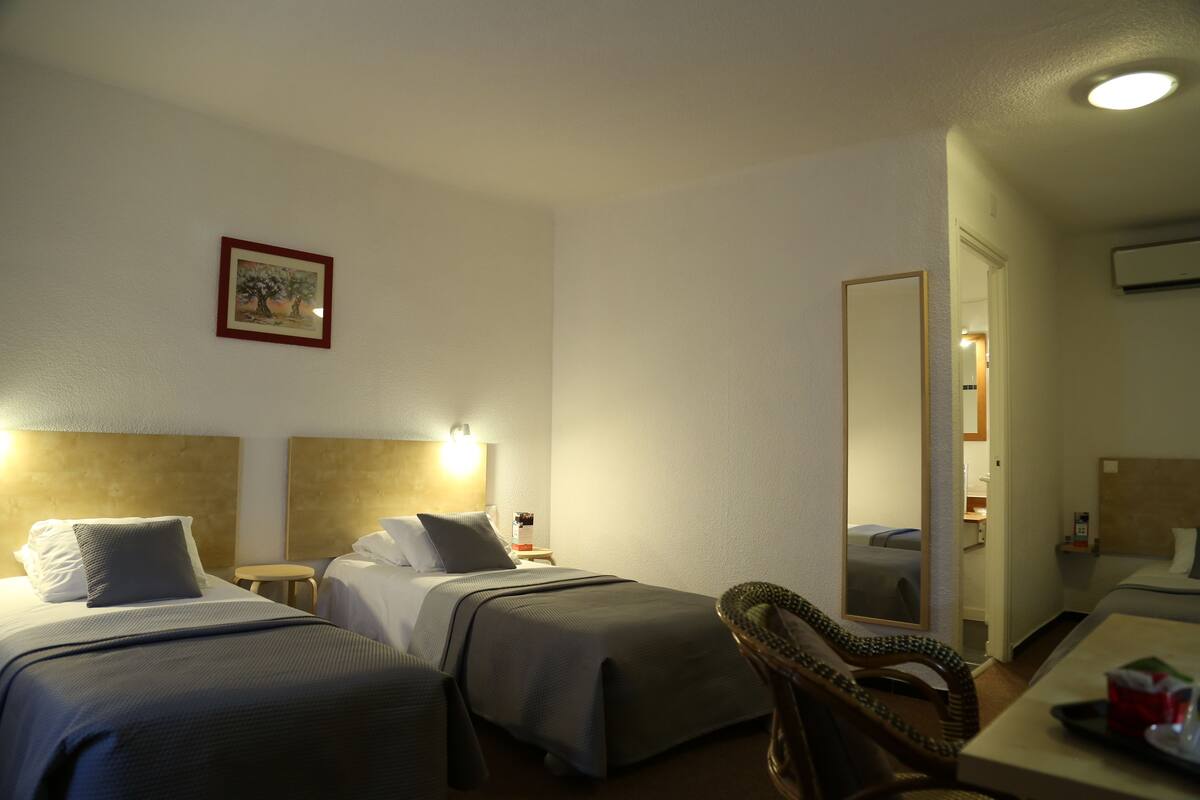 A hotel room with two beds, a small table, a chair, and a mirror.