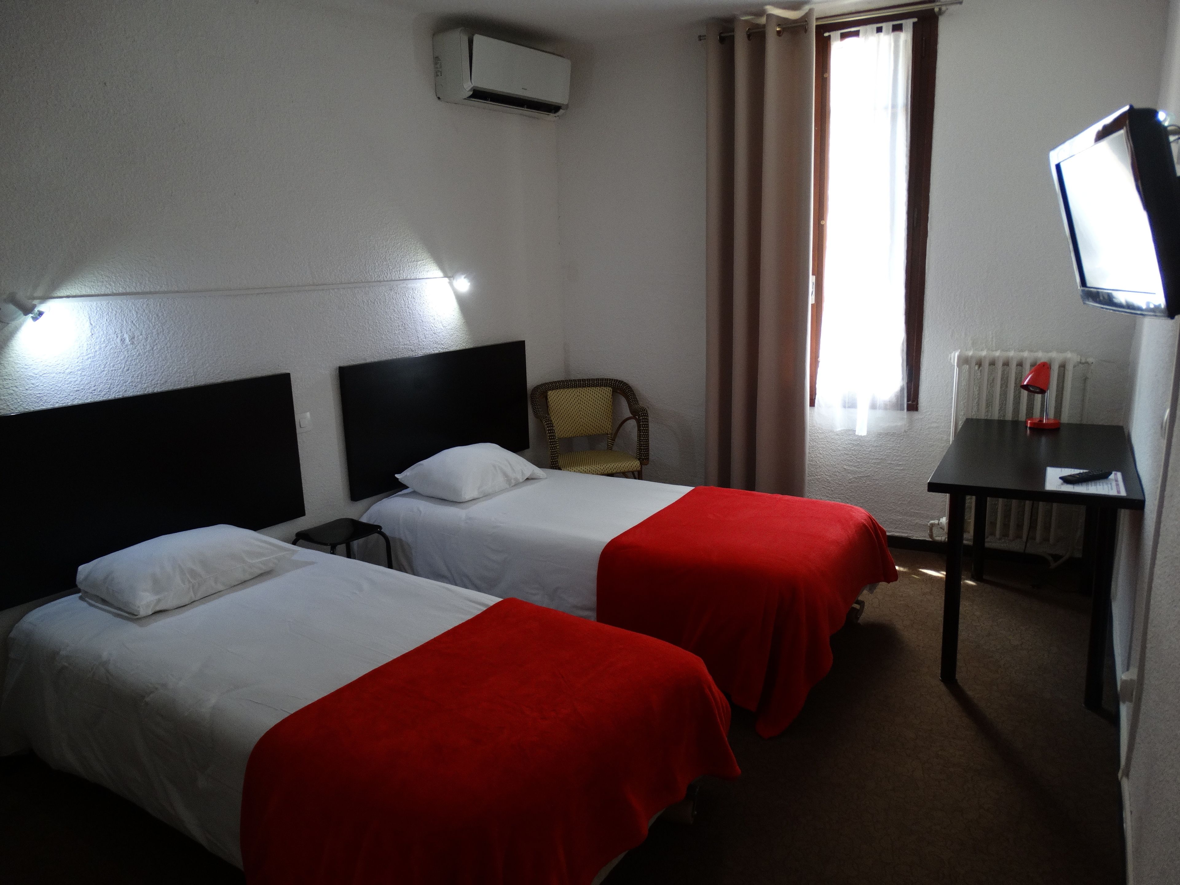 Une chambre d’hôtel avec deux lits, une chaise, un bureau, un téléviseur et un appareil de climatisation.