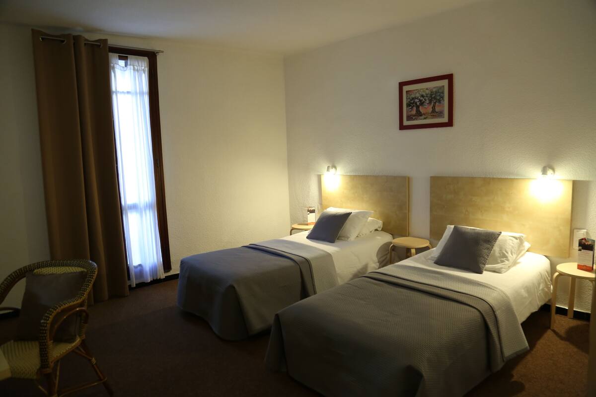 A hotel room with two single beds, a chair, and a nightstand with a lamp.