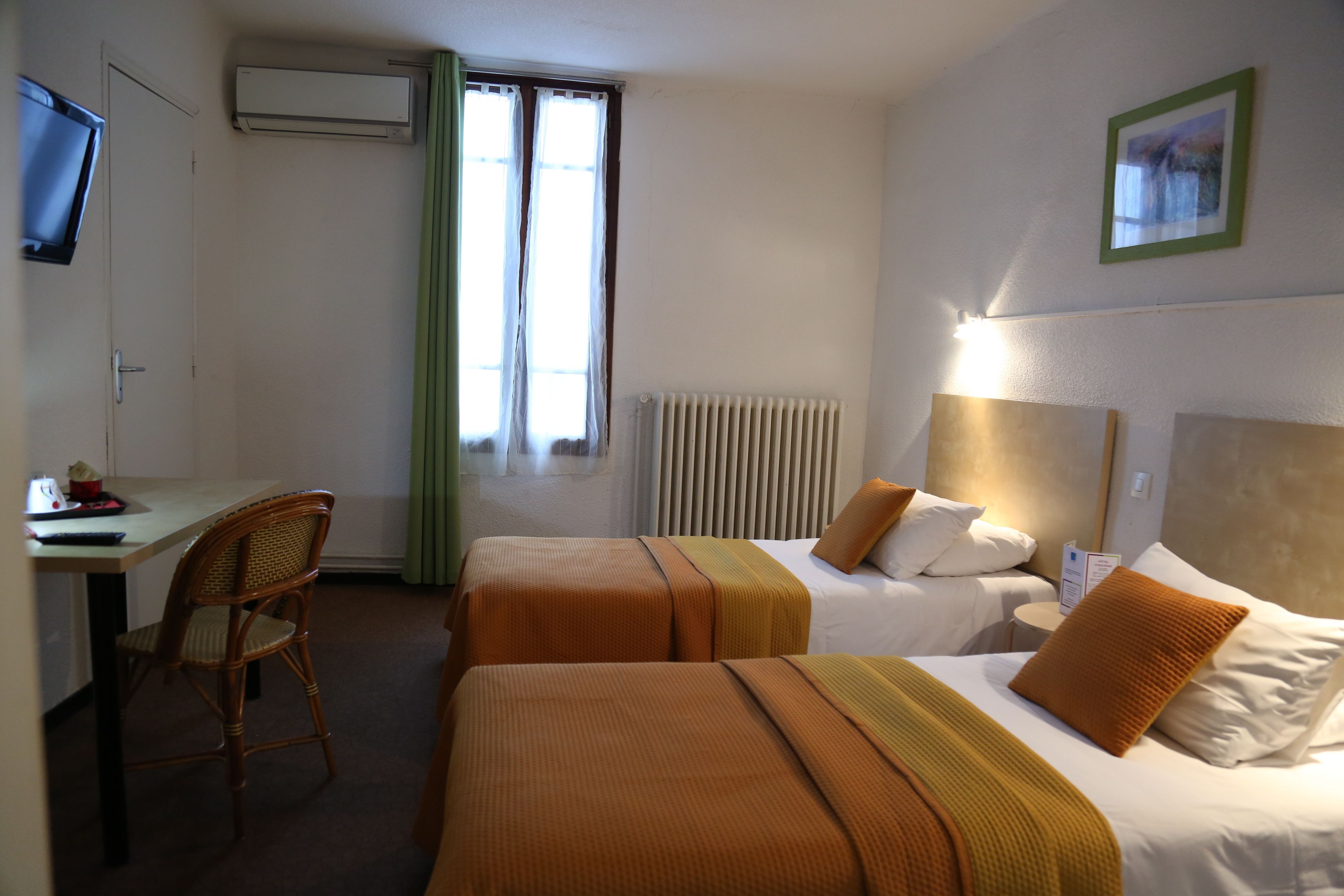 A hotel room with two beds, a desk, a chair, and a television.