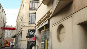 Una calle con un edificio que tiene un gran ventanal y un letrero que dice 'Galeries Lafayette'.