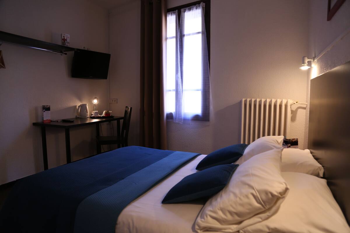 A hotel room with a bed, a desk, a chair, a television, and a window with curtains.