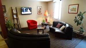 Una sala de estar con un sofá de cuero negro, un sillón rojo y un televisor en la pared.