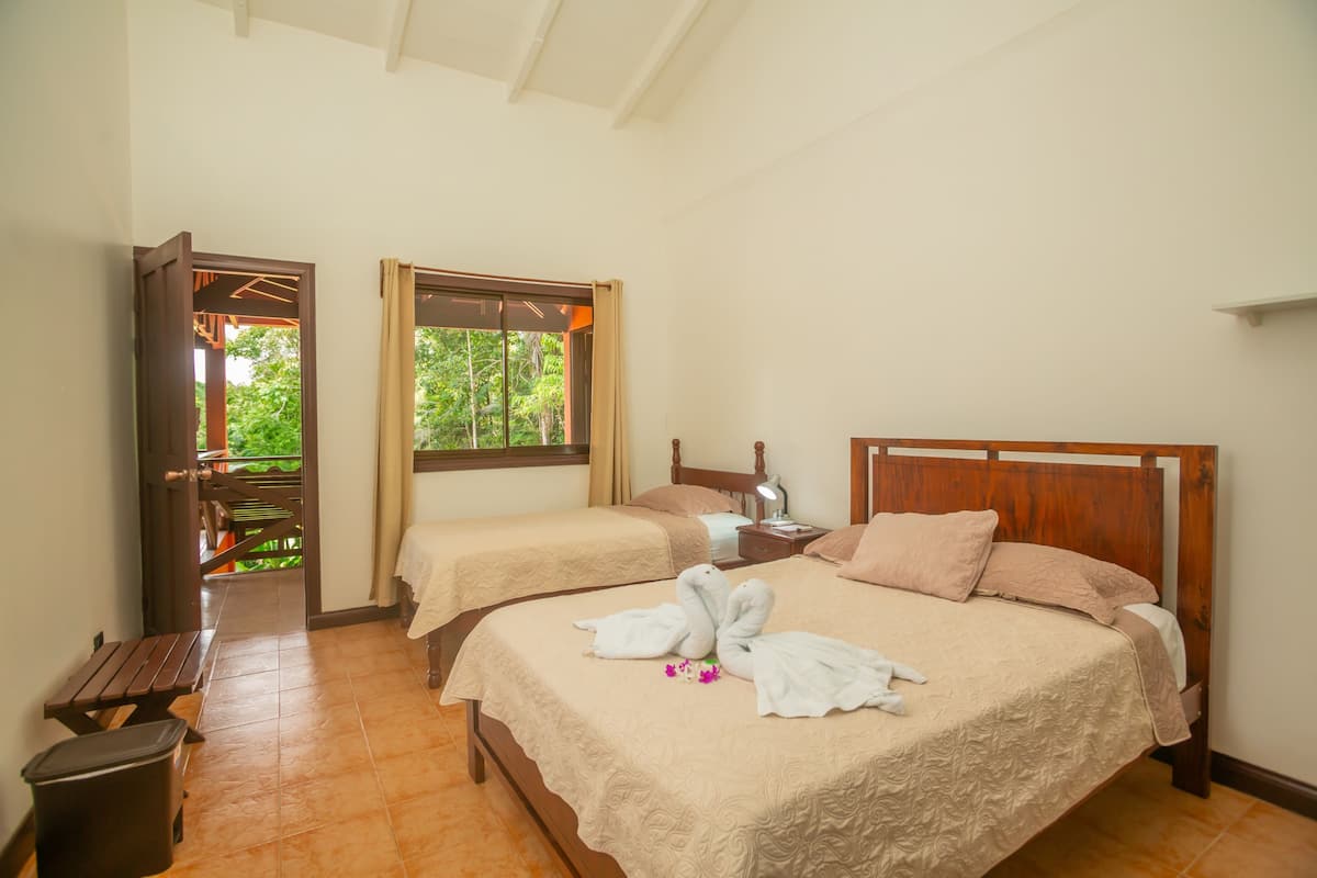 Habitación de hotel con dos camas, cabecera de madera, mesita de noche, escritorio y ventana con cortinas.