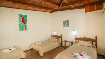 A hotel room with two single beds, a wooden headboard, a small bedside table with a lamp, and artwork on the walls.