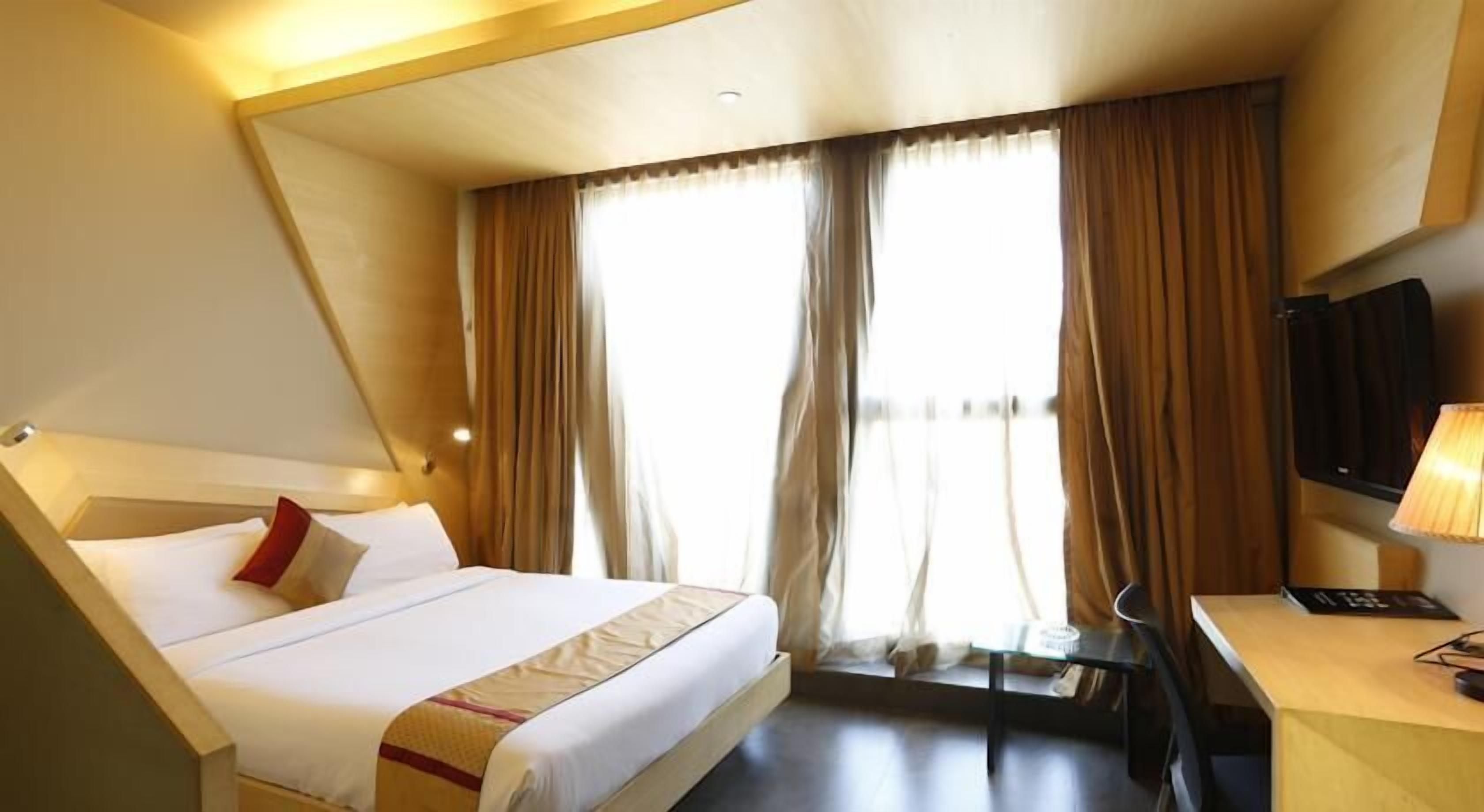 Een hotelkamer met een bed, een bureau, een televisie en een raam met gordijnen.