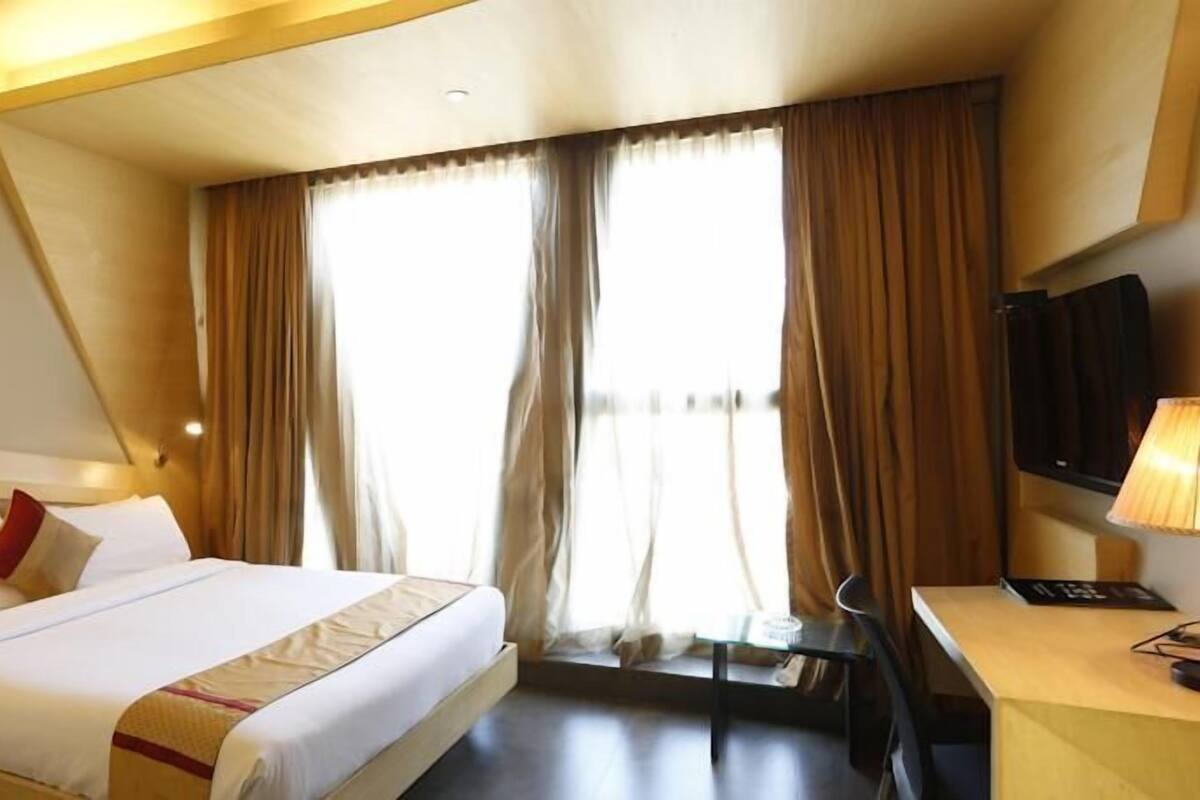Ein Hotelzimmer mit Bett, Schreibtisch, Fernseher und einem fensterbepflanzten Fenster.