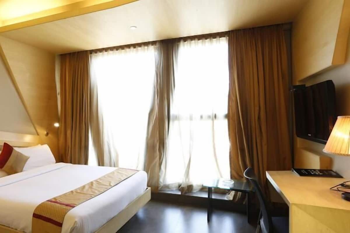 A hotel room with a bed, a desk, a TV, and a window with curtains.