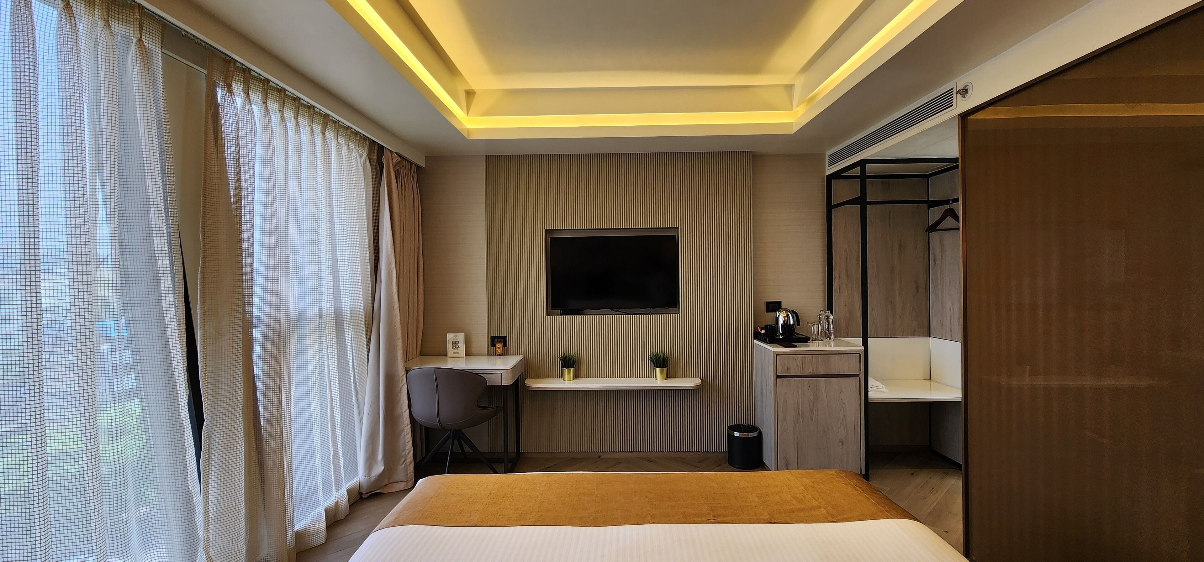 A hotel room with a bed, desk, chair, TV, and a small kitchenette.