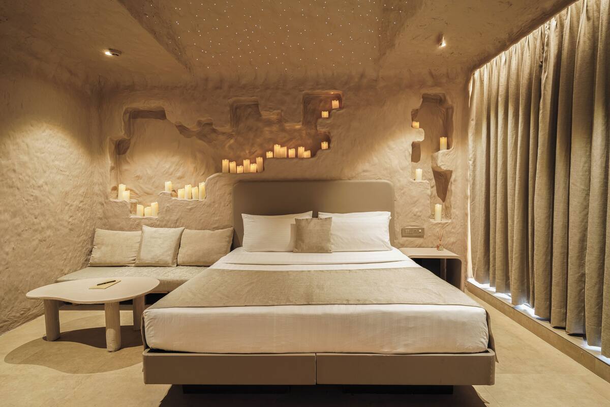 Ein geräumiges Schlafzimmer mit einem großen Bett, einem Nachttisch und einem Beistelltisch. Das Zimmer zeichnet sich durch eine außergewöhnliche Wandgestaltung aus Stein und ein Fenster mit Vorhängen aus.