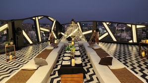 Une terrasse sur le toit dotée d’un sol aux motifs géométriques, un espace de restauration central avec une table dressée pour deux personnes, et une vue sur le paysage urbain.