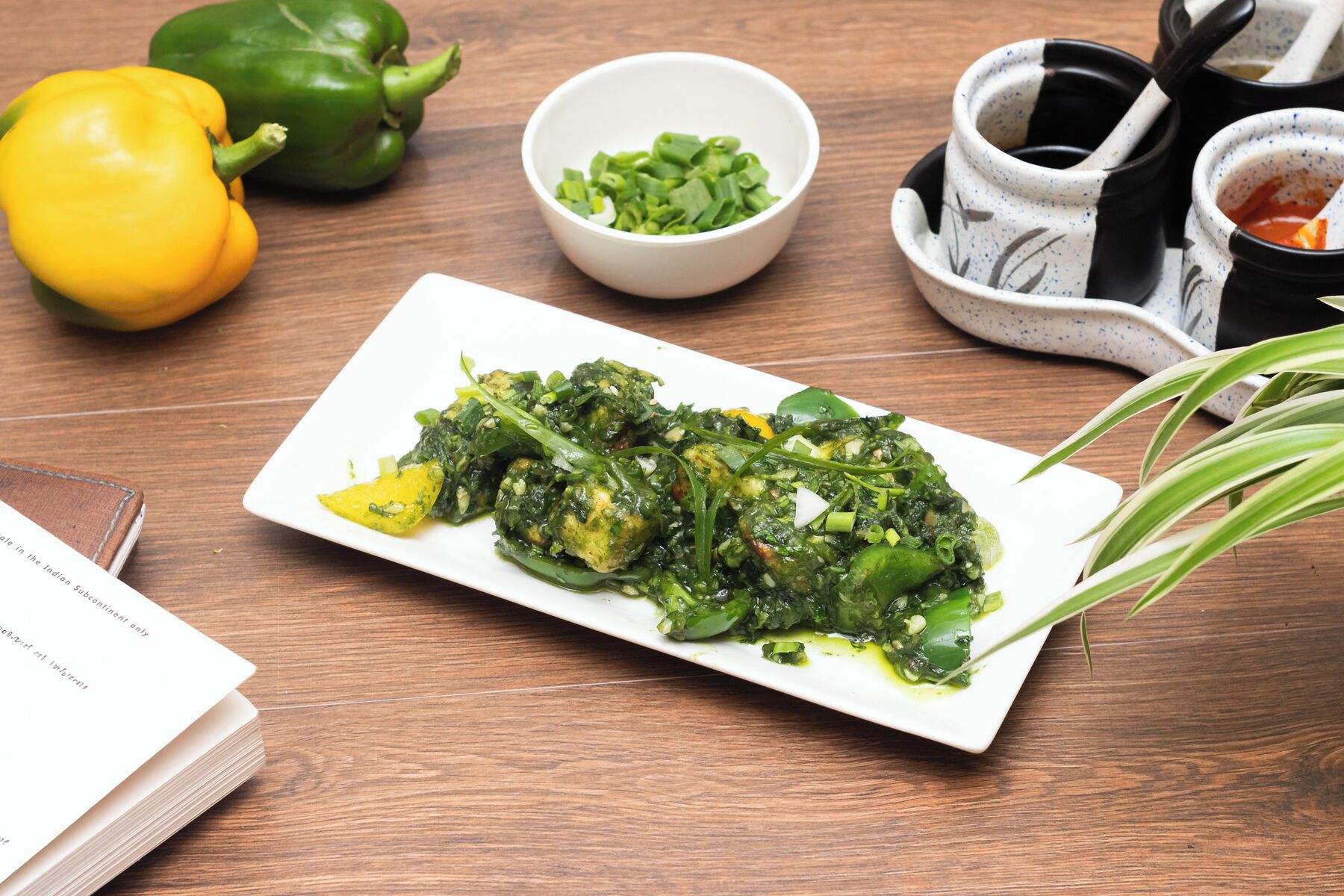 A plate of cooked greens with a yellow bell pepper, green bell pepper, and chopped green onions on a wooden table.