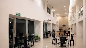 A modern dining area with multiple tables and chairs, a fire exit sign, and a view of the kitchen in the background. - Nantra Silom (Bangkok)