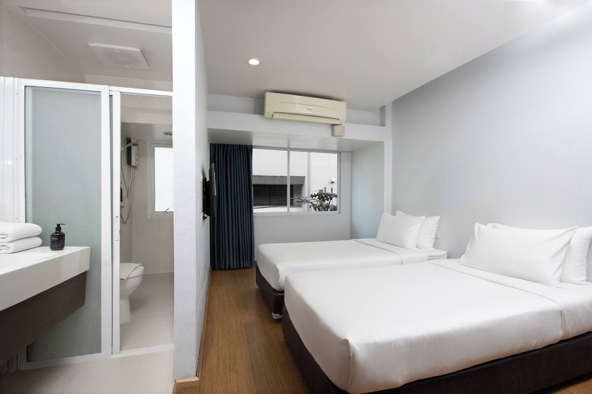 Ein Hotelzimmer mit zwei Betten, einem Badezimmer mit Toilette und Waschbecken sowie einem Fenster mit Blick.