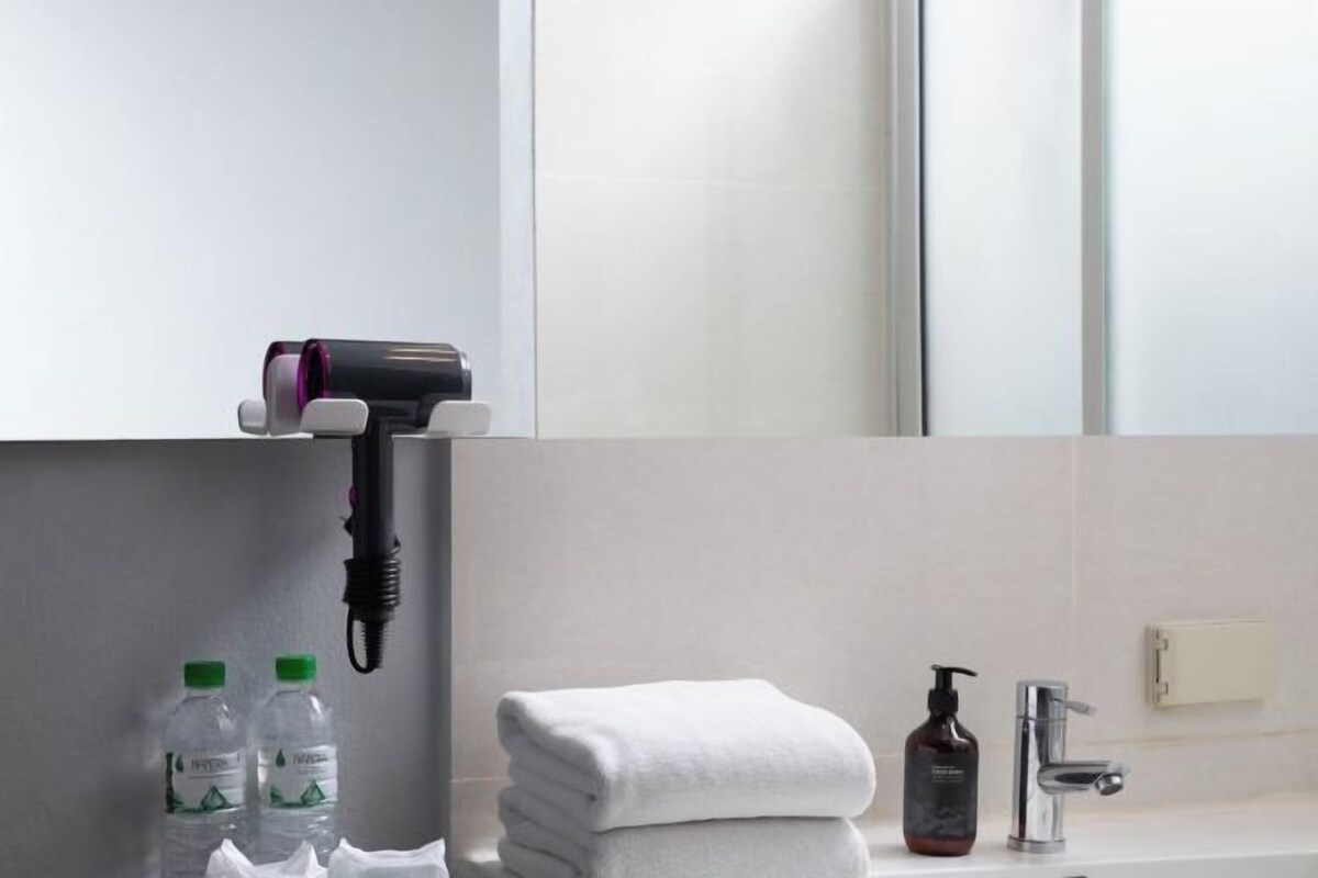 Casa de banho com pilha de toalhas, secador de cabelo e duas garrafas de água.