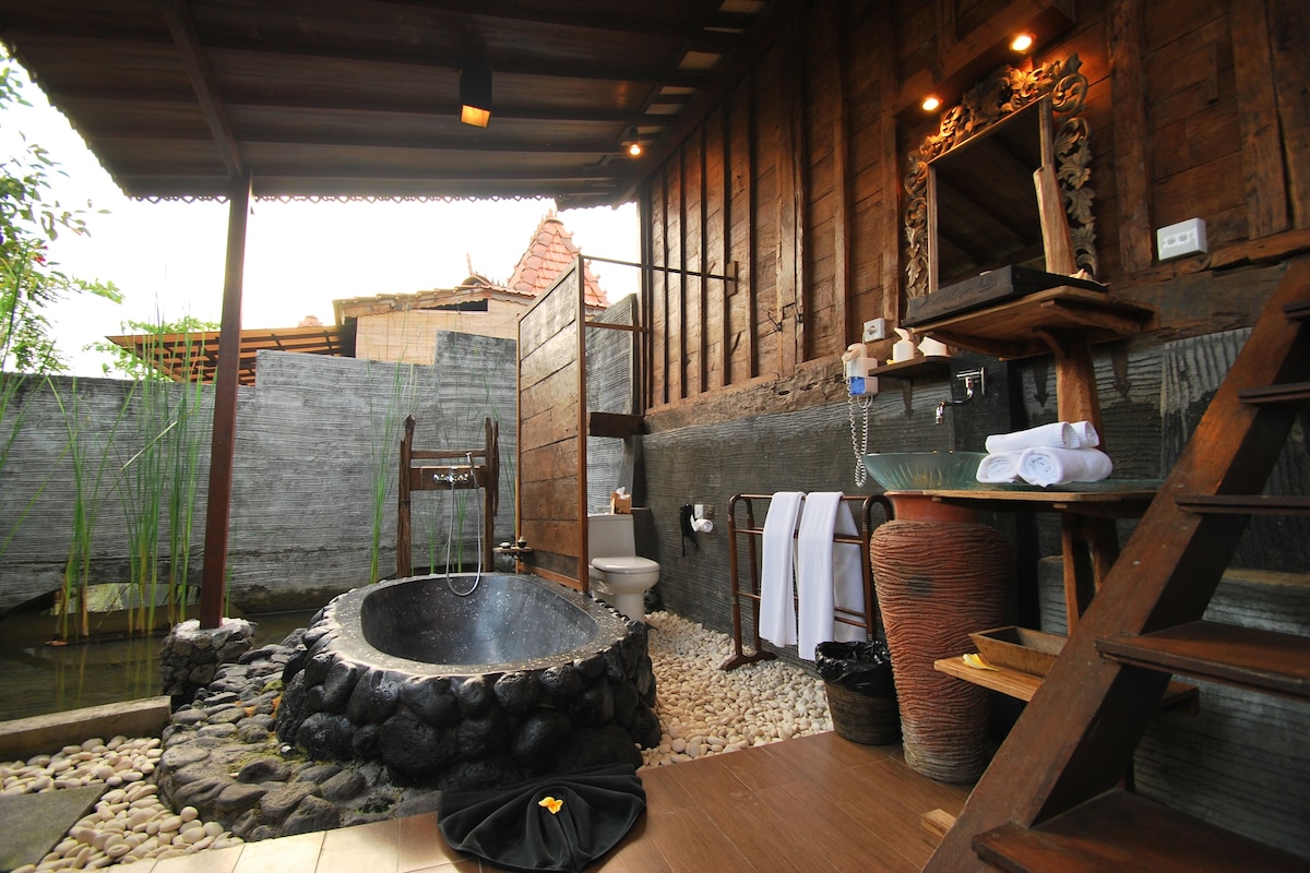 Un baño rústico con una bañera de piedra, estantes de madera y revestimiento exterior de madera.