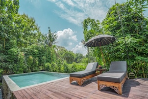 Un patio in legno con piscina, due poltrone prendisole e un ombrellone.