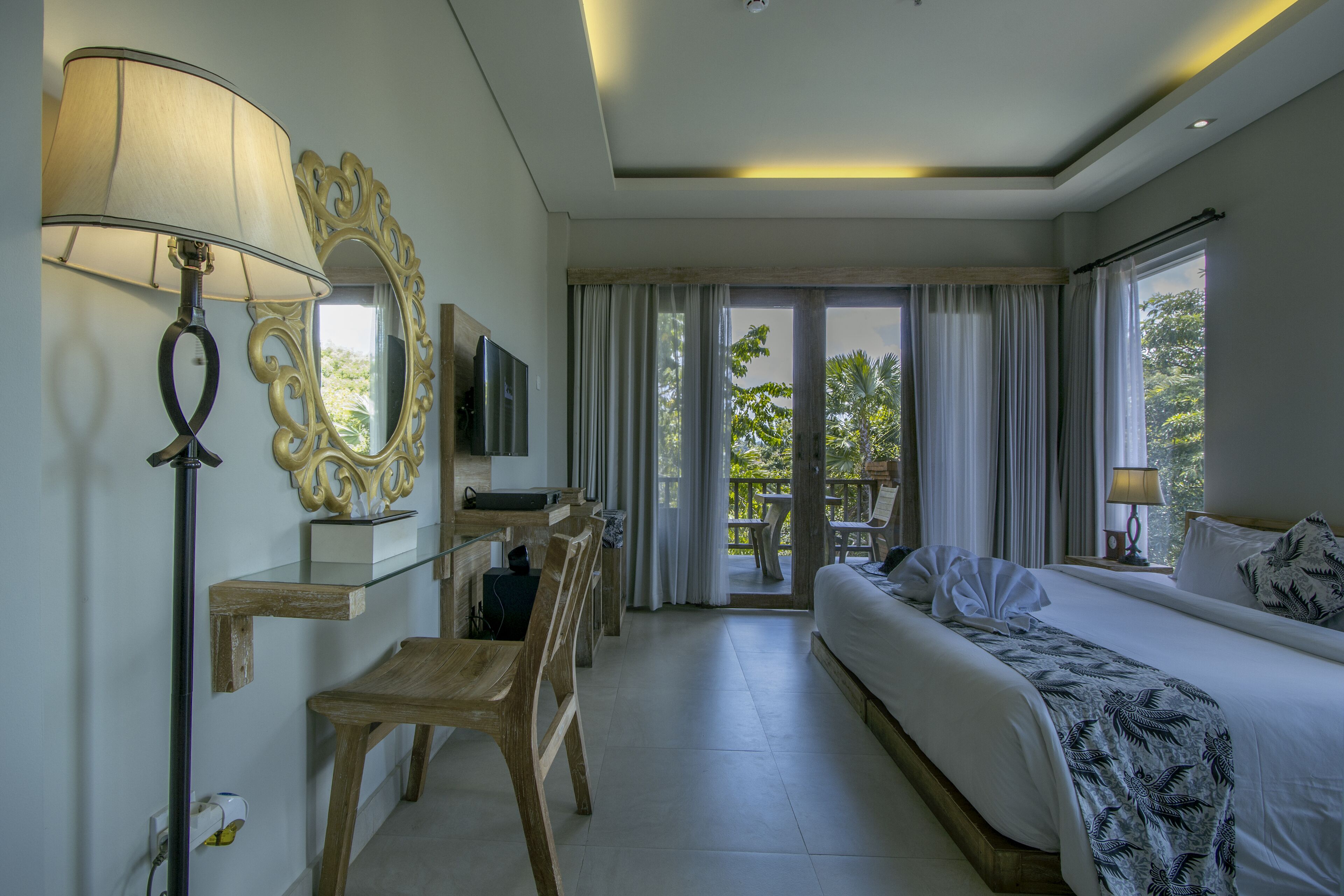 A hotel room with a bed, a desk, a chair, a TV, and a balcony with curtains.