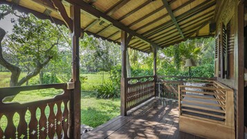 Una terrazza in legno con tetto di paglia, immersa nel verde e circondata da alberi.