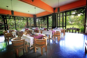 Un'ampia sala da pranzo interna con tavoli e sedie, e grandi finestre che offrono vista sull'esterno.