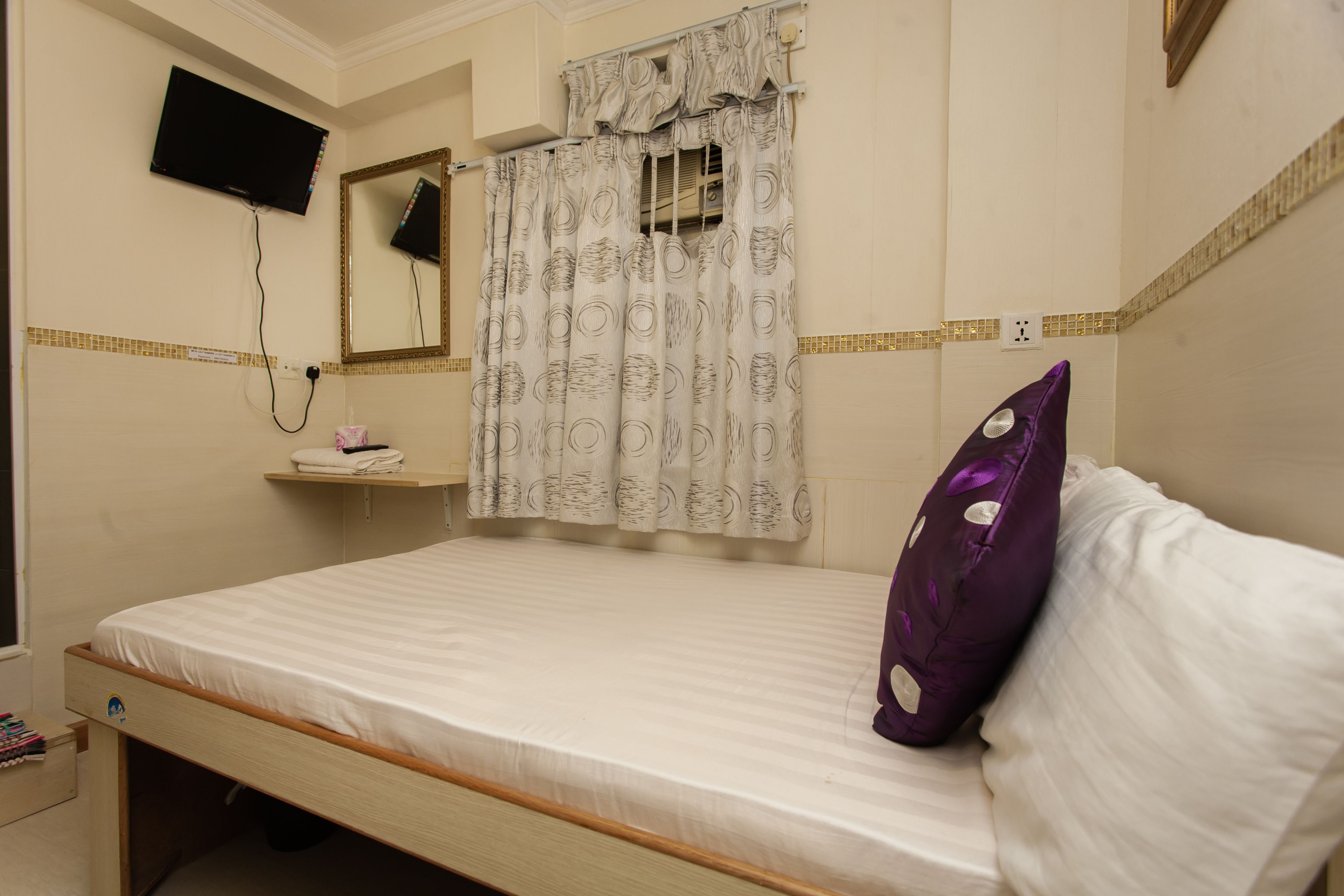 A bedroom with a bed, a television mounted on the wall, a mirror, and a shower curtain.