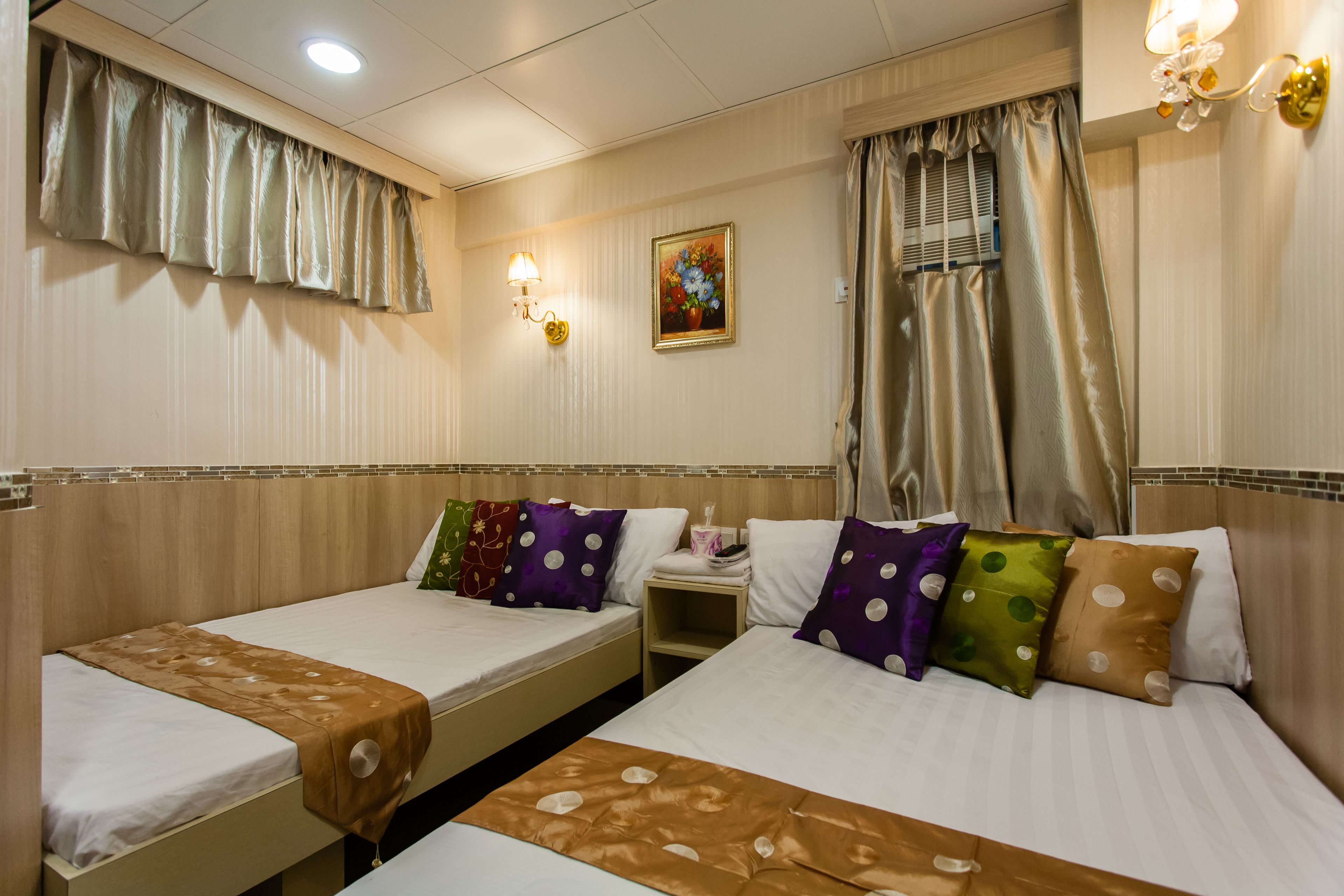 A hotel room with two single beds, a nightstand, a painting, and a window with curtains.