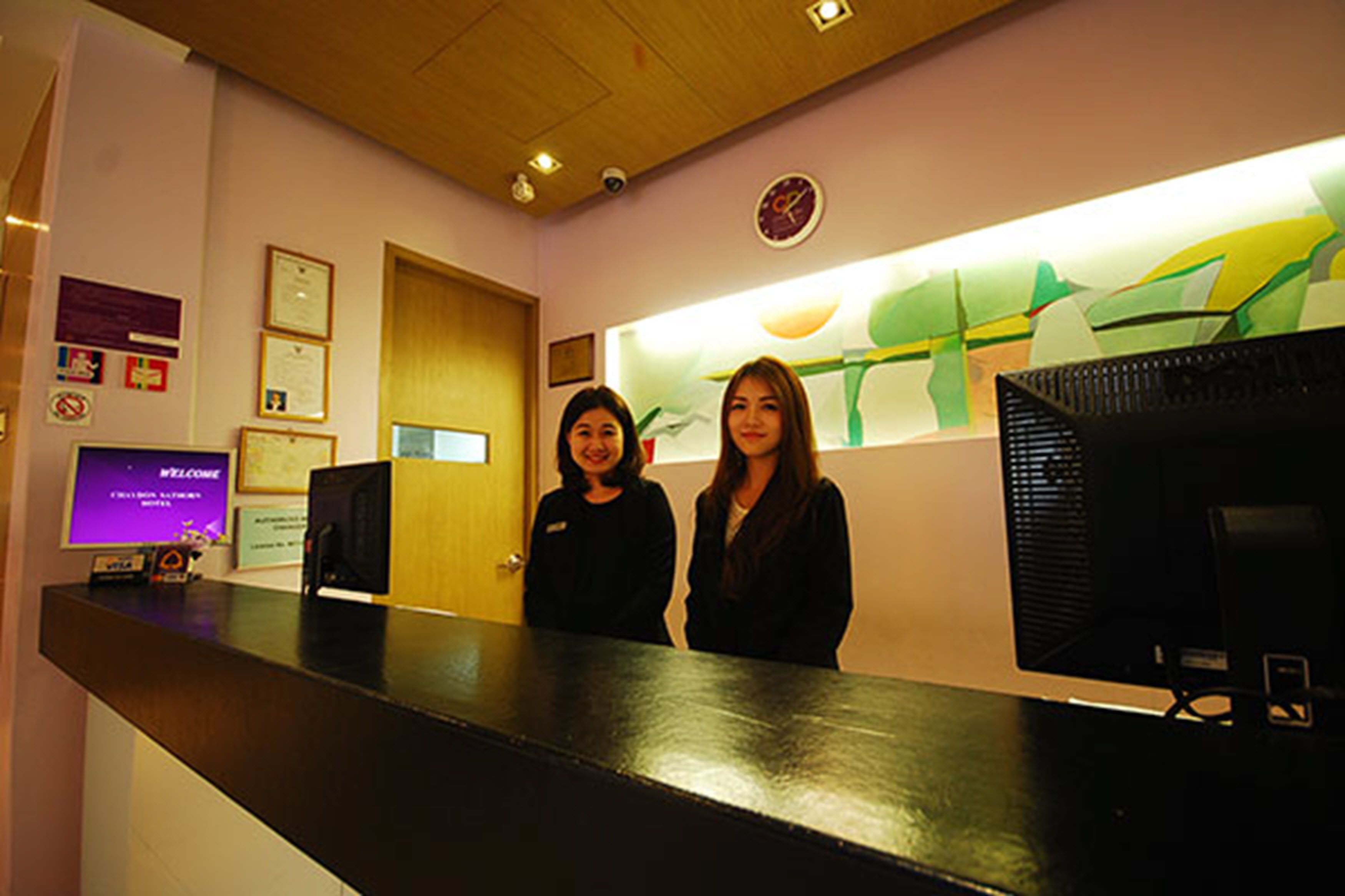 Zona de recepción con mostrador, dos empleados, un reloj y certificados enmarcados en la pared.
