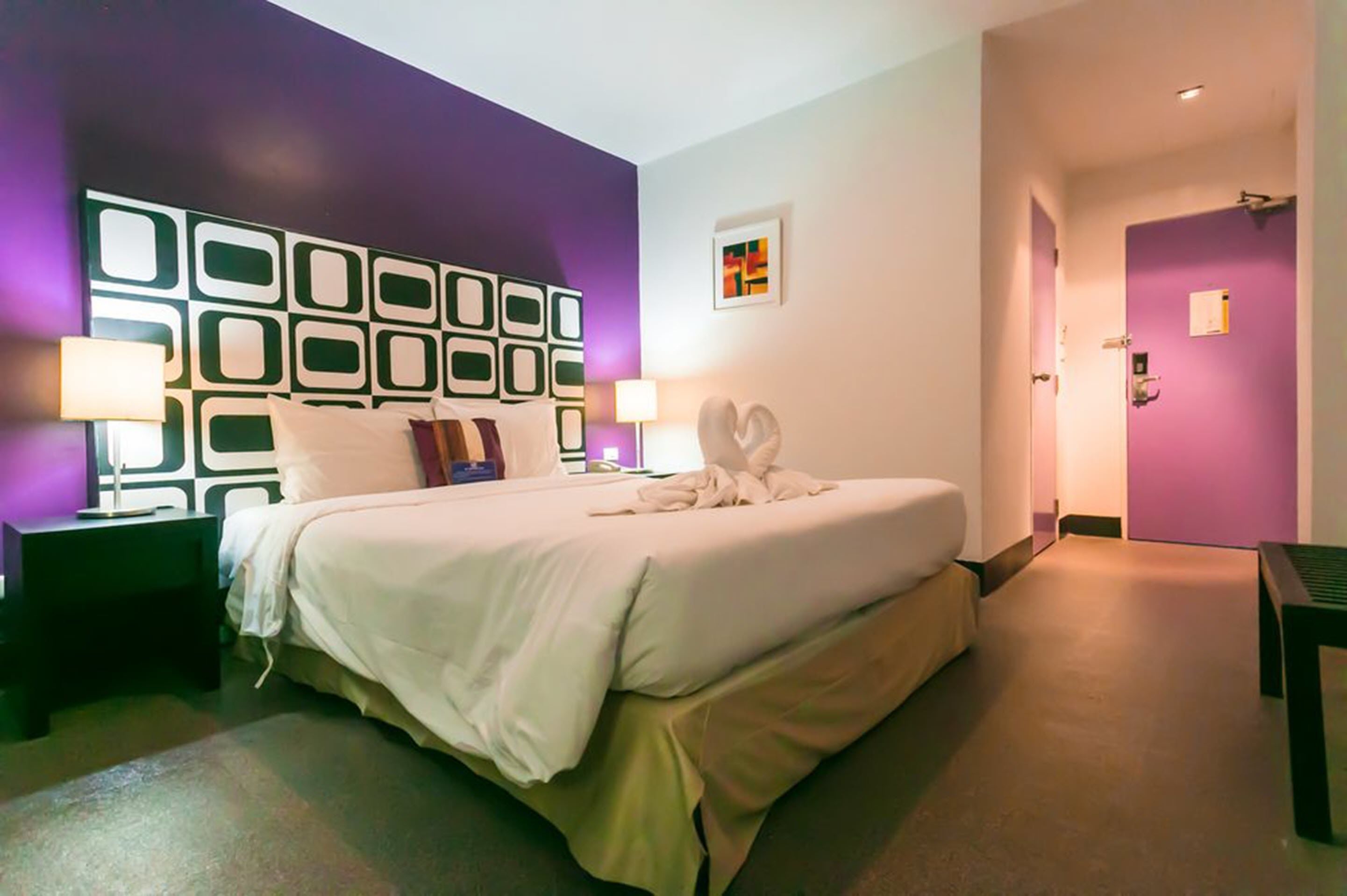Ein Hotelzimmer mit einem großen Bett, zwei Nachttischen, einem Kopfteil mit geometrischem Muster und einer violetten Akzentwand.