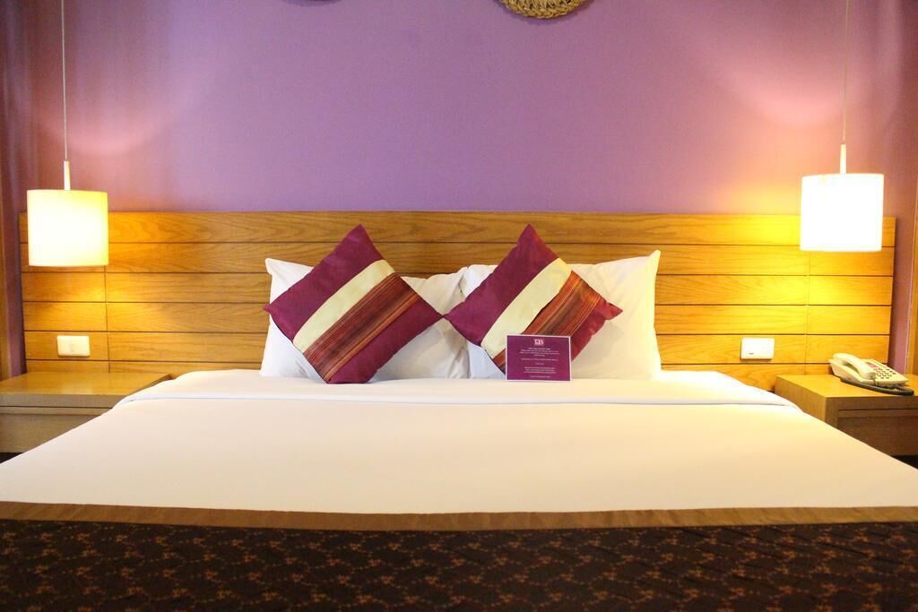 A hotel room with a large bed, two nightstands, a telephone, and a wall-mounted lamp.